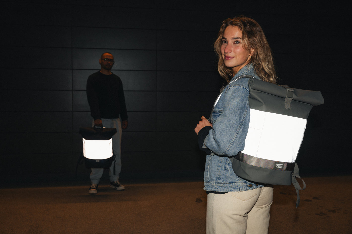 Frau mit reflektierendem grauen Rucksack und Mann mit reflektierender schwarzer Tasche bei Nacht