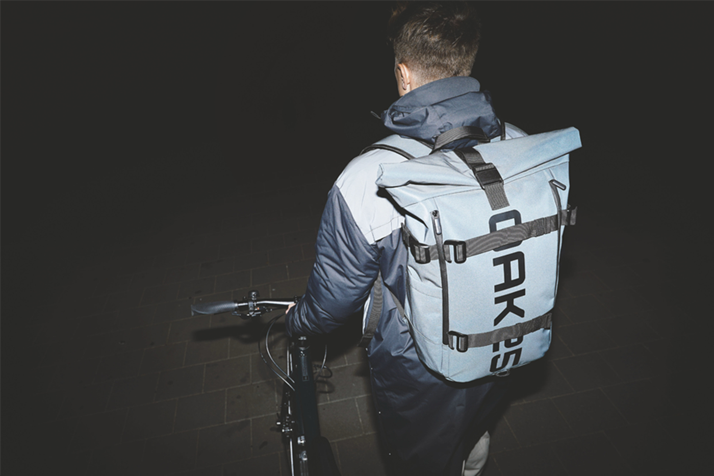 Person mit blau-grauem OAK25 Rucksack und Fahrrad bei Dunkelheit